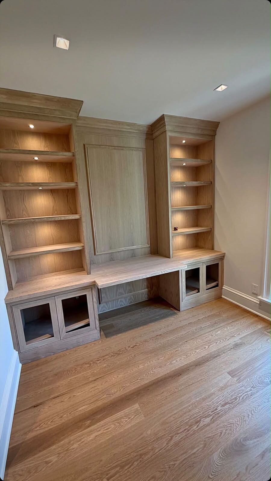 White oak built-ins with a center desk, lit shelving and glass-front cabinets